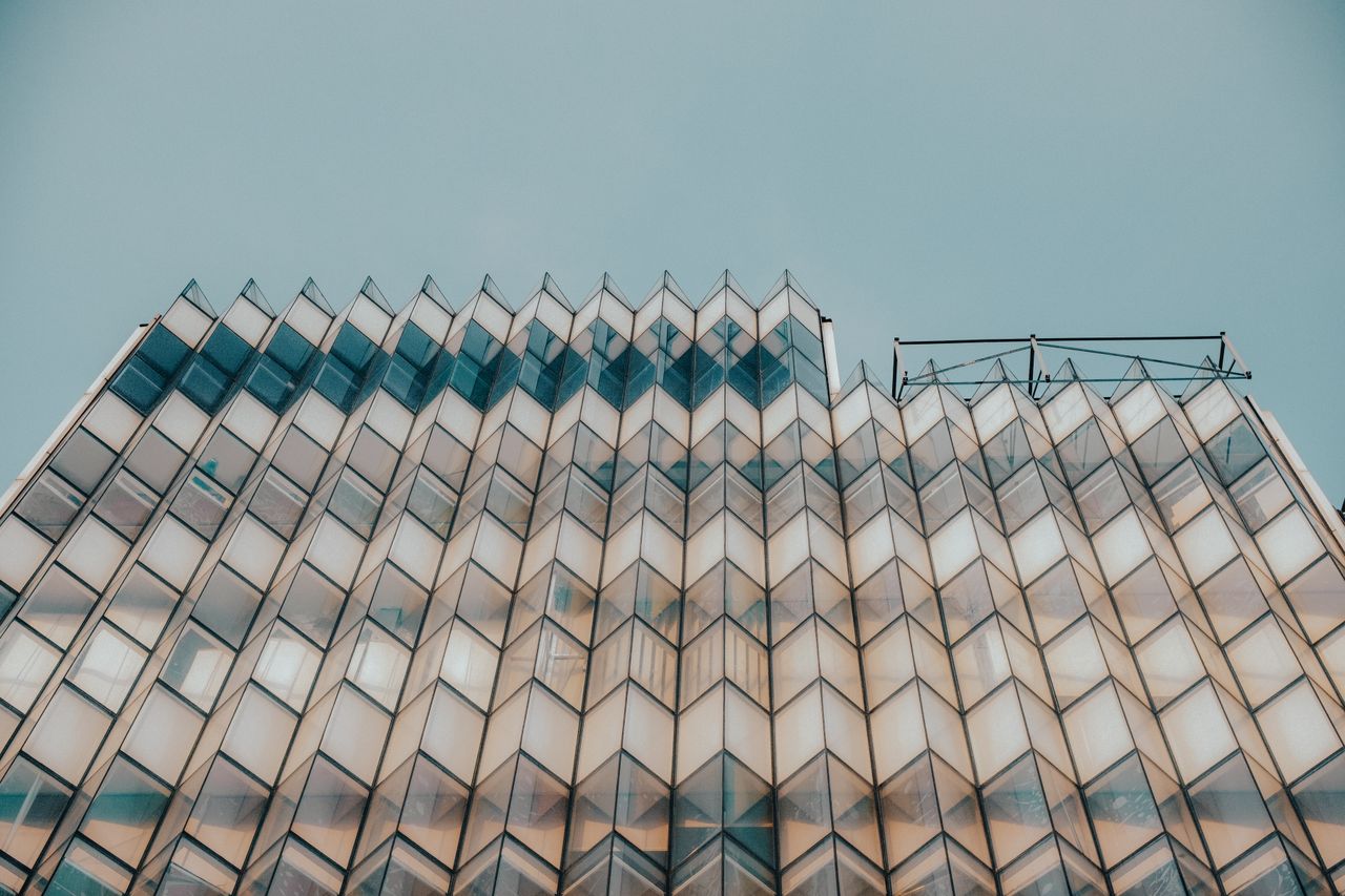 Upward view of a modern building's glass facade with a distinctive geometric pattern under a clear sky.